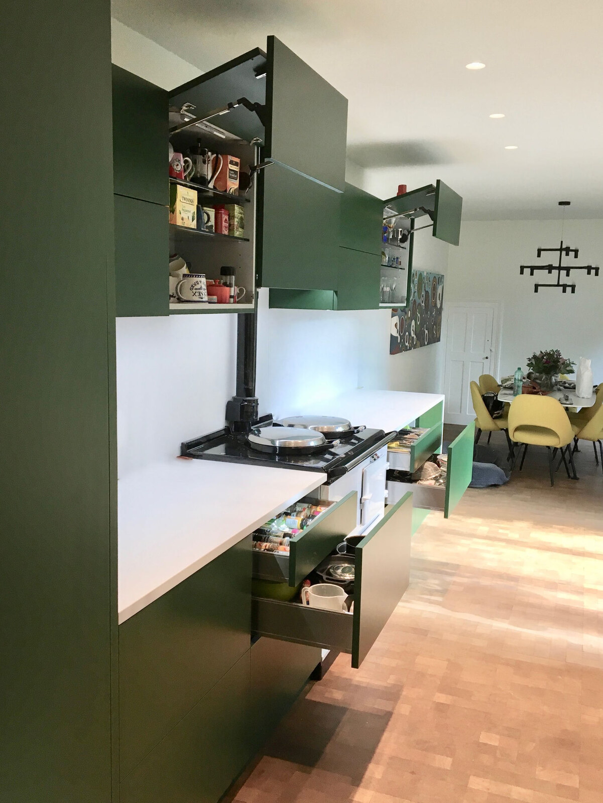 Green kitchen with lift-up wall units and pull-out drawers open showing contents