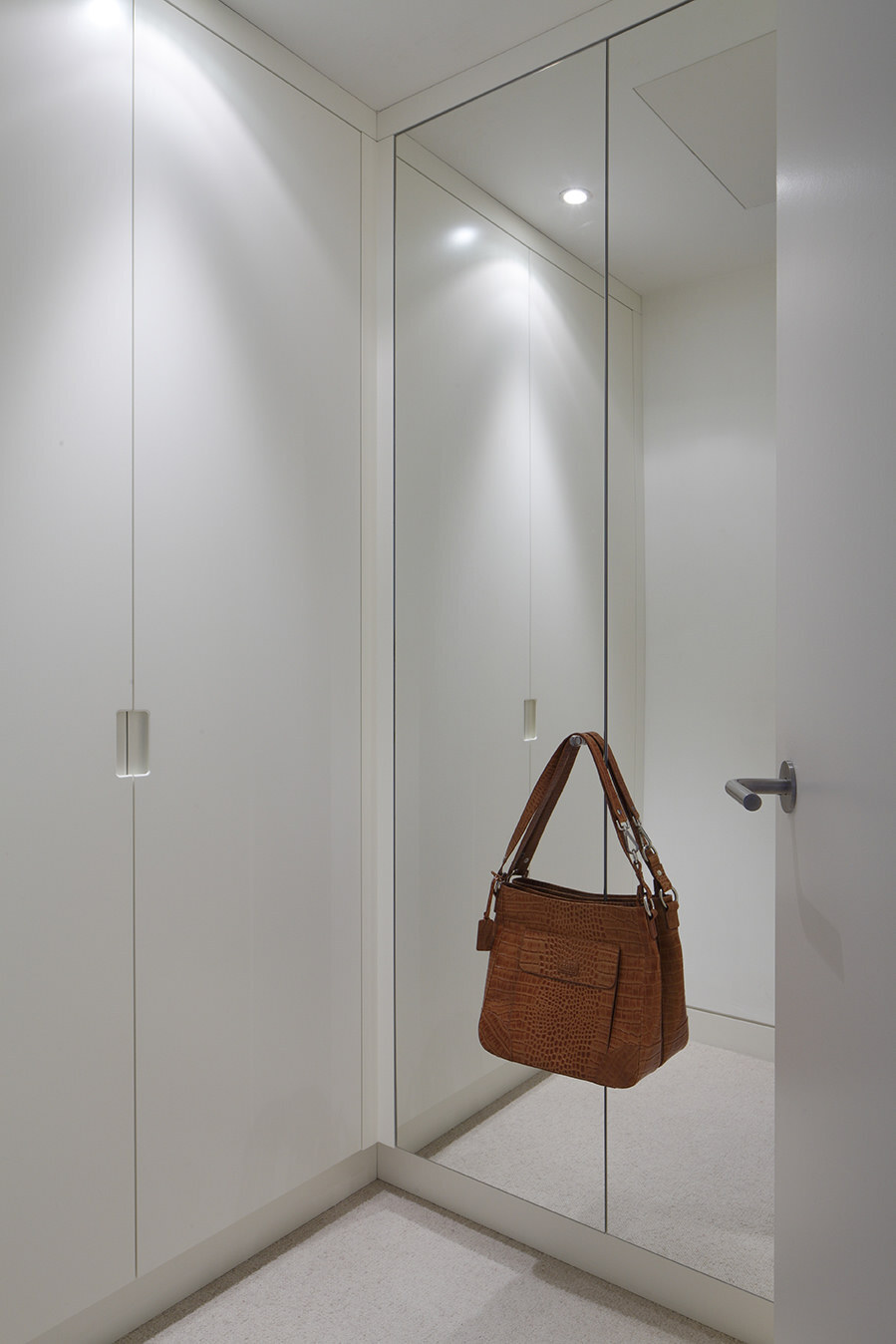 Bespoke walk-in wardrobe with handleless white doors and full-height mirror