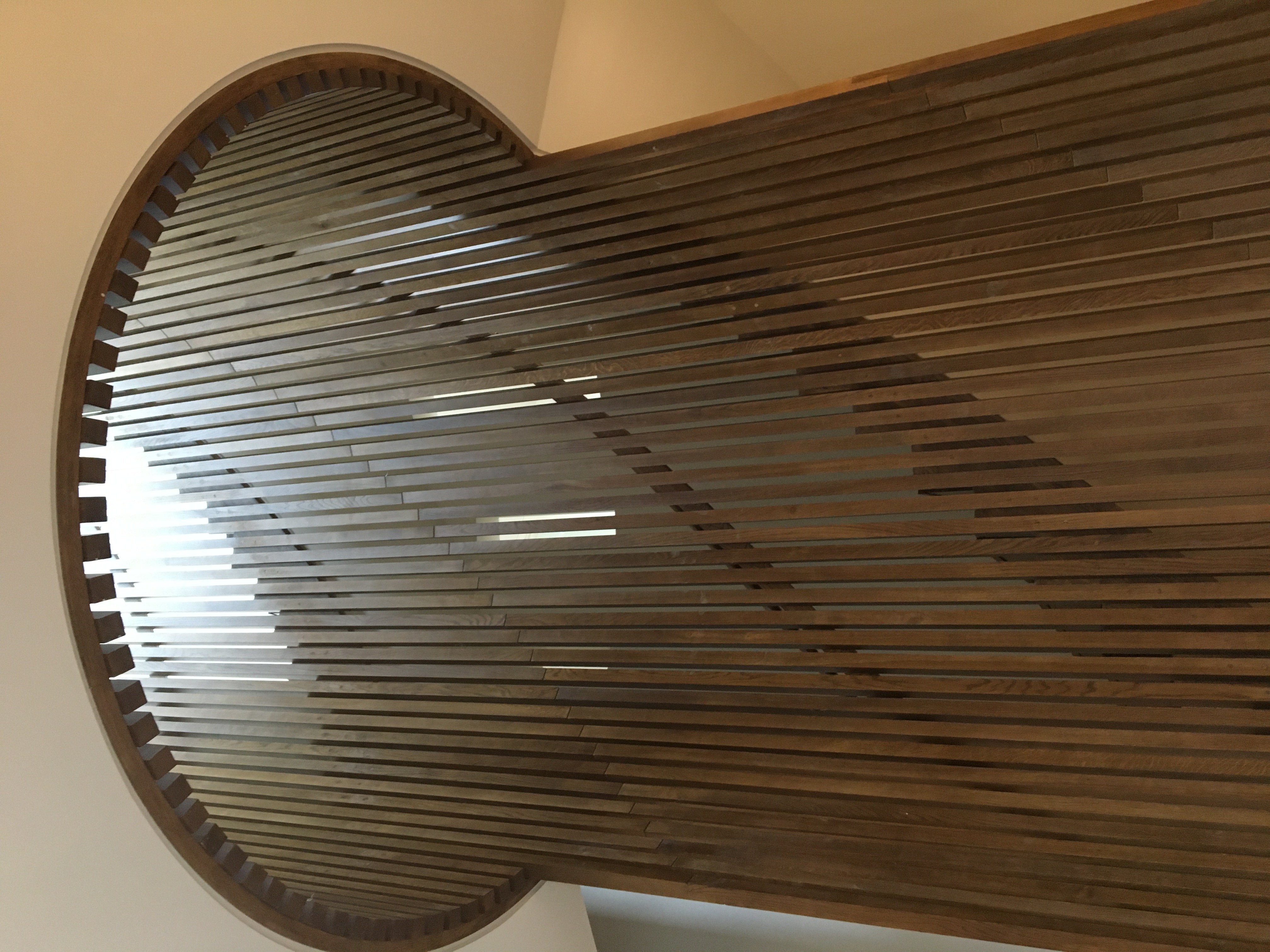 Curved walnut vertical slatted staircase enclosure with circular skylight and reflected light
