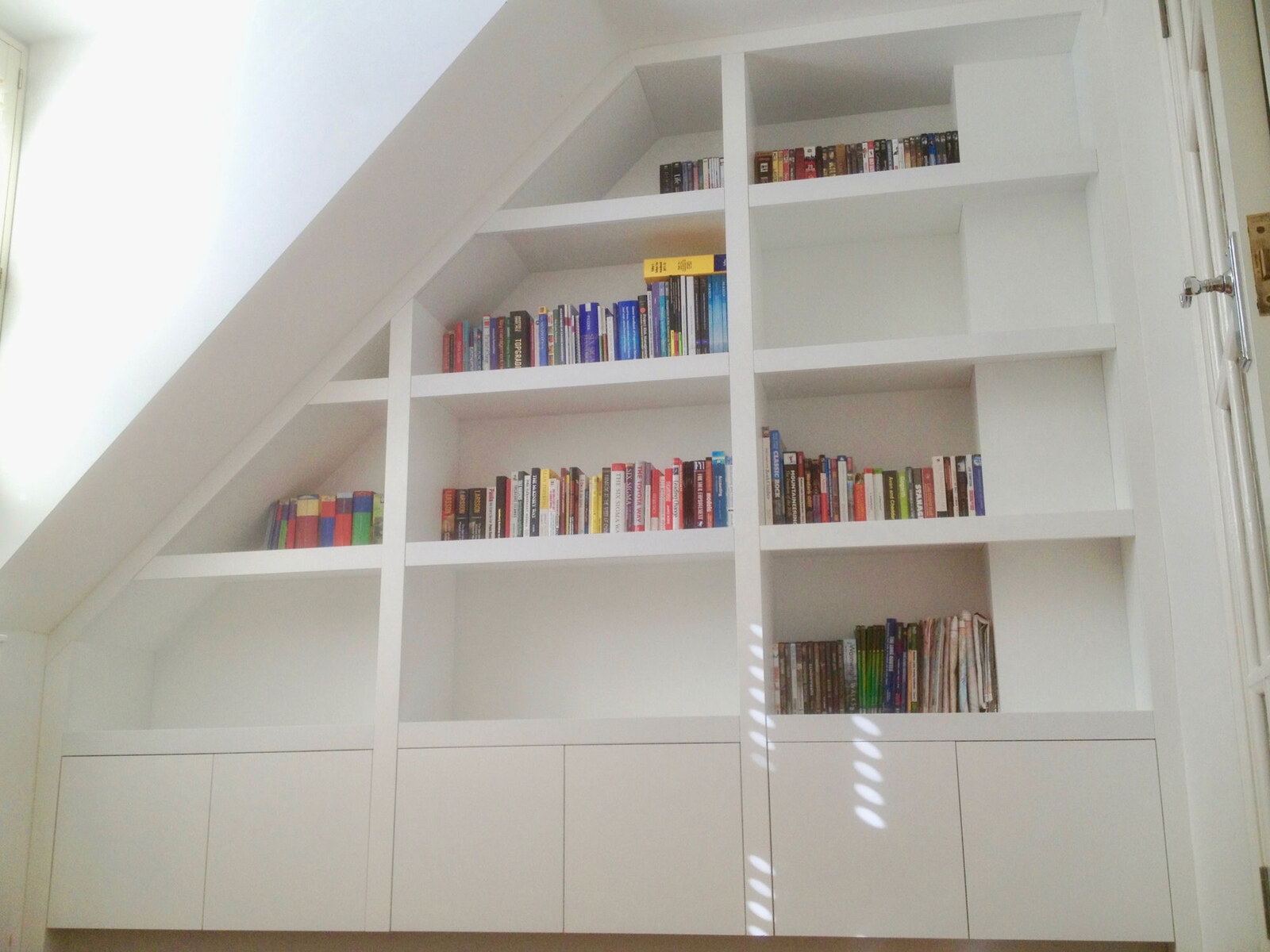 Bespoke white attic bookcase with cupboards under a sloping ceiling